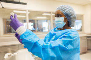 ĻӰ Bernard J. Dunn School of Pharmacy student in blue scrubs, gloves, cap and mask, holding a vial.